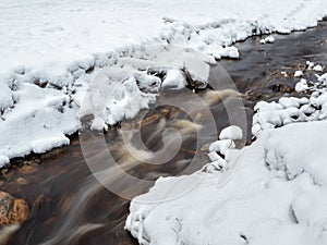 Winter mountain stream in Karelia flows through the forest. The power of wild majestic nature. Water turbulence