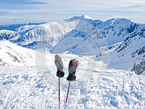 Winter mountains and ski gloves on ski poles on foreground