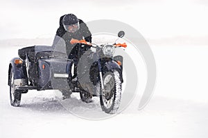 A winter nature trip on a motorcycle with a side trailer. A man pushes a bogged motorcycle out of a snowdrift. Blizzard.