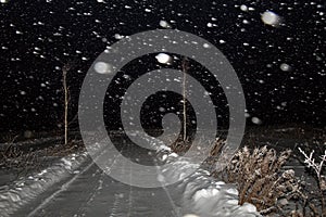 Winter night landscape with road in a field in the snow. The snowfall, blizzard and the dark sky