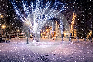 Winter night park with lanterns and Christmas decorations in snowfall