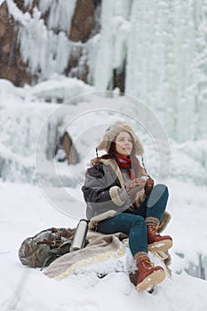 Winter outdoor recreation. Young woman drinks hot tea from thermos