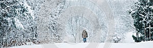 Winter outdoor scene landscape. Man walking under snow in park. Heavy snowfall and snowstorm. Snow blizzard and bad weather winter