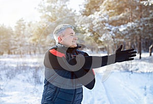 Winter outdoor workout concept. Cheerful mature guy doing warmup exercises before his run in snowy winter forest