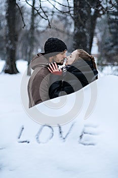 Winter outdoors portrait of Young couple in love and word Love on snow. Valentines day outdoors celebration date ideas