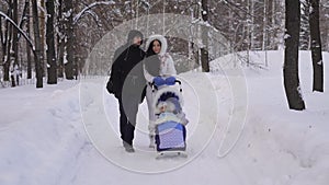 Winter Park. The couple spend time with a child in the park. Woman in warm jacket rolls the stroller with the child. A