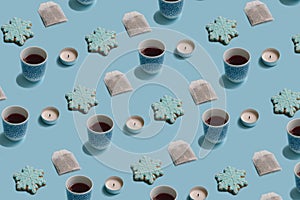 Winter pattern made of teabag, cup, candle and snowflake cookie on pastel blue background. Minimal concept arrangement