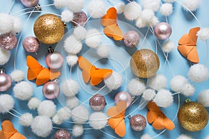 Winter pattern with white balls, orange paper butterflies, golden glitter balls on blue background