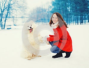 Winter and people - happy smiling young woman owner having fun with white Samoyed dog outdoors