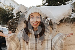Winter photo of happy young caucasian woman looking at camera with smile on face against snowy wall.