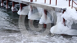 Winter pier on the shore of an unfrozen lake with ice and waves