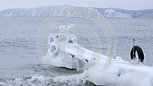 Winter pier on the shore of an unfrozen lake with ice and waves