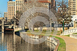 Winter pond with park pathway and sidewalk in late afternoon sun in city with skyscraper office building background