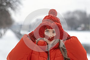 Winter portrait of a beautiful young woman in red hat. Girl shows heart sign with her palms in gloves