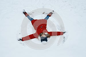 Winter portrait of cheerful girl having fun in the snow, lying on the snow in the form of angel, top view