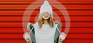 Winter portrait of cheerful woman pulls a hat over her eyes wearing white hat with pom pom on red