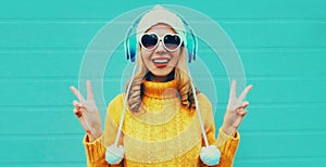 Winter portrait cheerful young woman in wireless headphones listening to music wearing yellow knitted sweater and white hat