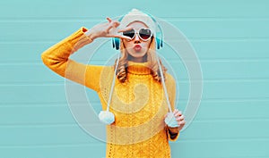 Winter portrait cool young woman in wireless headphones listening to music blowing red lips wearing yellow knitted sweater