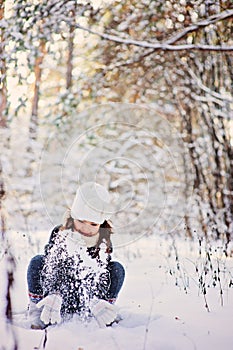 Winter portrait of cute happy child girl in grey fur coat plays with snow in forest