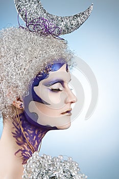 Winter portrait of a girl with creative make-up on a light background. Purple - Gold Makeup.