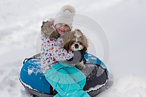 Winter portrait of a girl with a puppy on a tubing. A girl and a dog ride on a hill in the winter