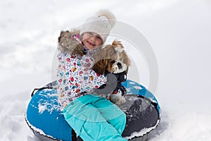 Winter portrait of a girl with a puppy on a tubing. A girl and a dog ride on a hill in the winter