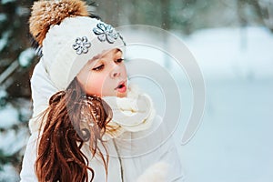 Winter portrait of happy child girl in white coat, hat and mittens playing outdoor in snowy winter forest