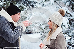 winter portrait of happy couple playing, blowing snow and spending good day outdoor in snowy forest