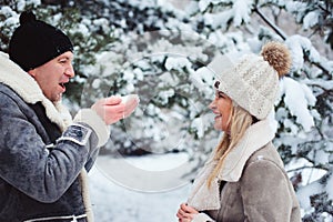 winter portrait of happy couple playing, blowing snow and spending good day outdoor in snowy forest.