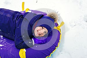 Winter portrait of a happy little boy in a hat. tired child sledding tubing