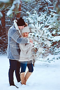 winter portrait of happy romantic couple warm up each other on the walk in snowy forest