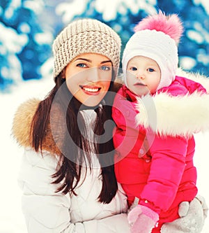 Winter portrait happy smiling mother and baby on hands over snowy christmas tree