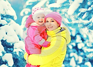 Winter portrait happy smiling mother holds baby on hands over snowy christmas tree