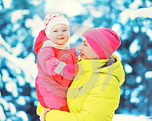 Winter portrait happy smiling mother holds baby on her hands over snowy christmas tree