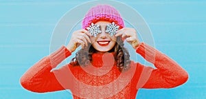 Winter portrait happy smiling young woman with snowflake wearing a knitted sweater, pink hat on blue background