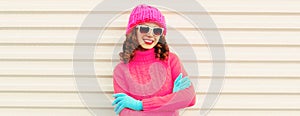 Winter portrait of happy smiling young woman wearing knitted sweater, pink hat on white background