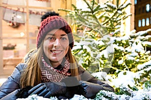 Winter portrait of happy young woman walking in snowy city decorated for Christmas and New Year holidays.