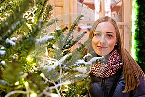 Winter portrait of happy young woman walking in snowy city decorated for Christmas and New Year holidays.