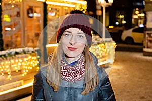 Winter portrait of happy young woman walking in snowy city decorated for Christmas and New Year holidays.