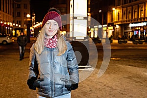 Winter portrait of happy young woman walking in snowy city decorated for Christmas and New Year holidays.