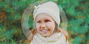 Winter portrait of little girl child wearing knitted hat sweater and scarf near christmas tree