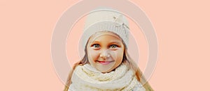 Winter portrait of little girl child wearing knitted hat, sweater and scarf on pink background