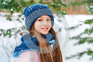 Winter portrait of a little happy girl with rosy cheeks in a sweater and a hat, a snowy landscape in the background