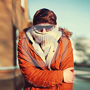 Winter portrait of man freezes hides his head and warms body in the city