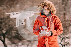 Winter Portrait of man wearing warm jacket flying drone, piloting white quadcopter