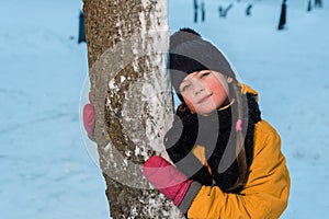 Winter portrait of a nice little girl near a tree. the child is wearing a winter hat