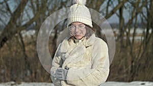 Winter portrait of a teenage girl in a knitted hat on which snow is falling.