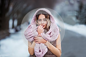 Winter portrait: Young pretty woman dressed in a warm woolen clothes, scarf and covered head posing outside.