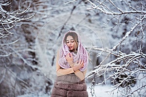 Winter portrait: Young pretty woman dressed in a warm woolen clothes, scarf and covered head posing outside.