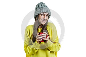 Winter portrait of young smiling positive woman in sweater, knitted hat with mug of hot drink, white background isolated